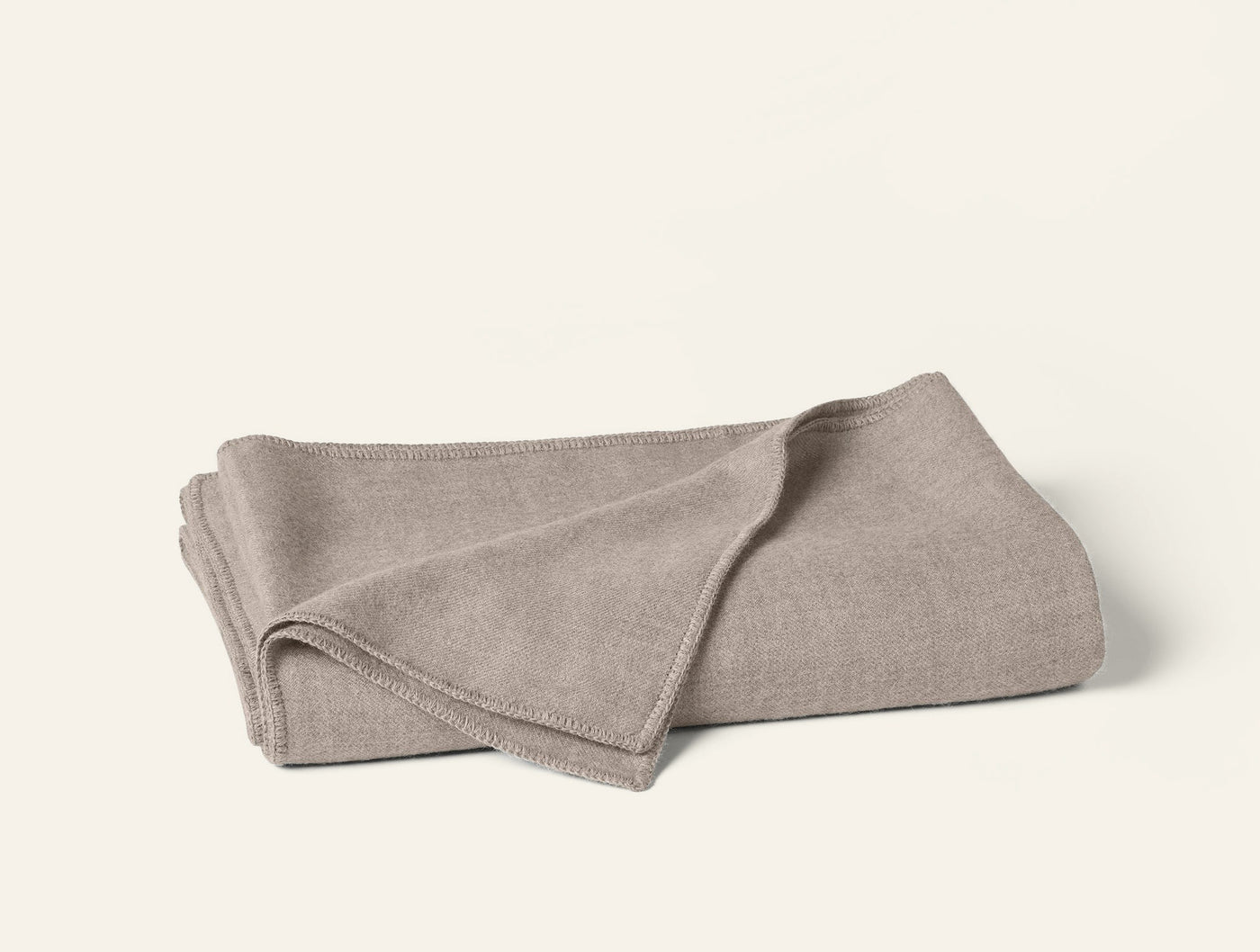 Folded oatmeal Coyuchi Pacaya blanket showing bound edge detail on white background.