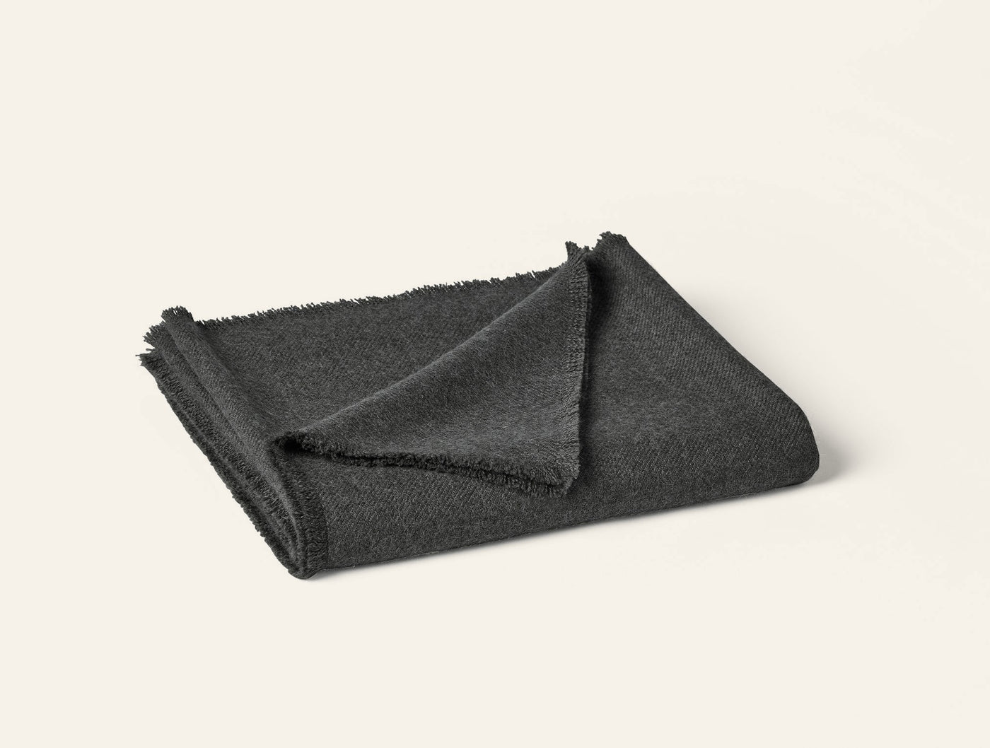 Folded charcoal alpaca throw with frayed hem detail, shot against white background.