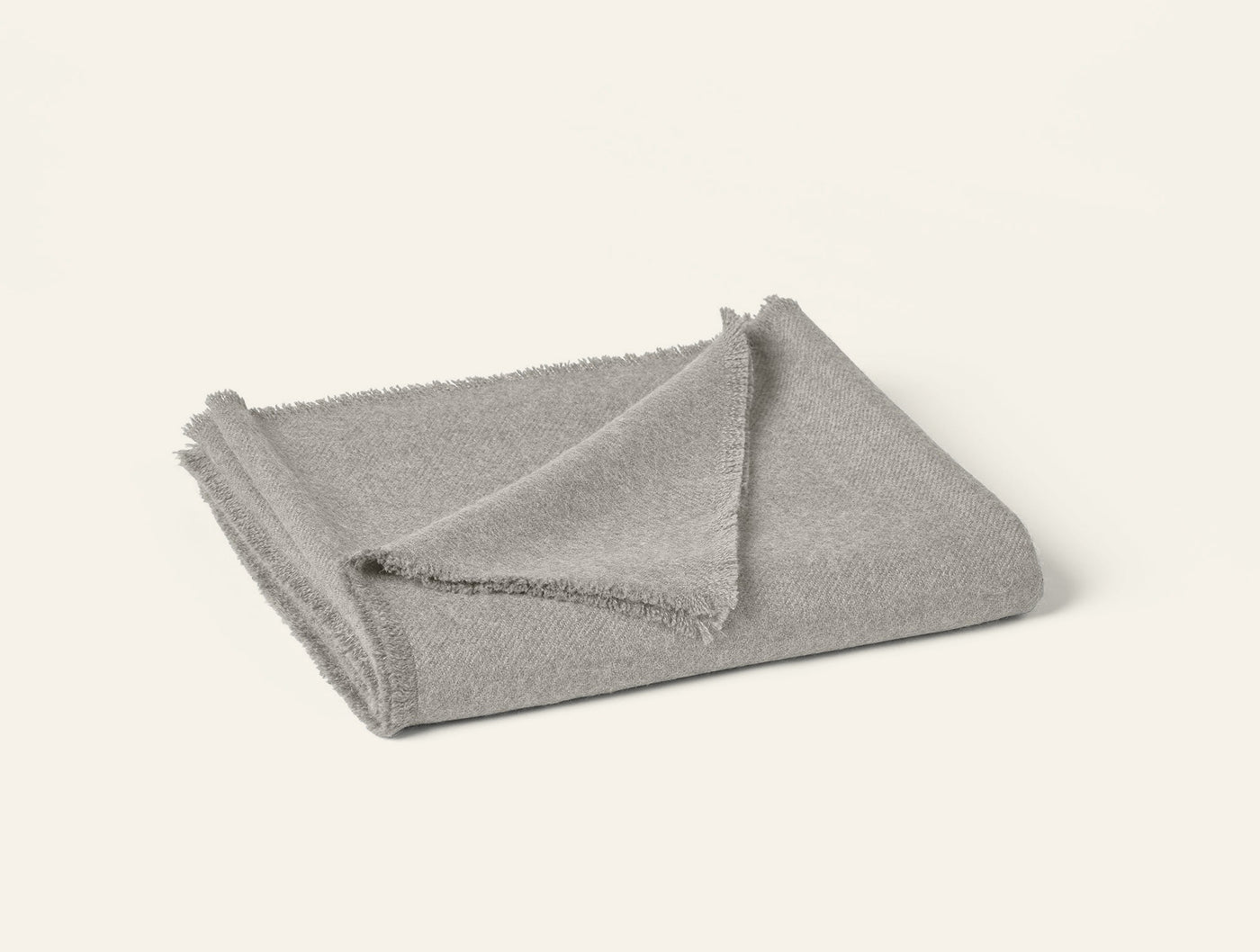 Folded silver grey alpaca throw with fringe trim detail, angled top view.