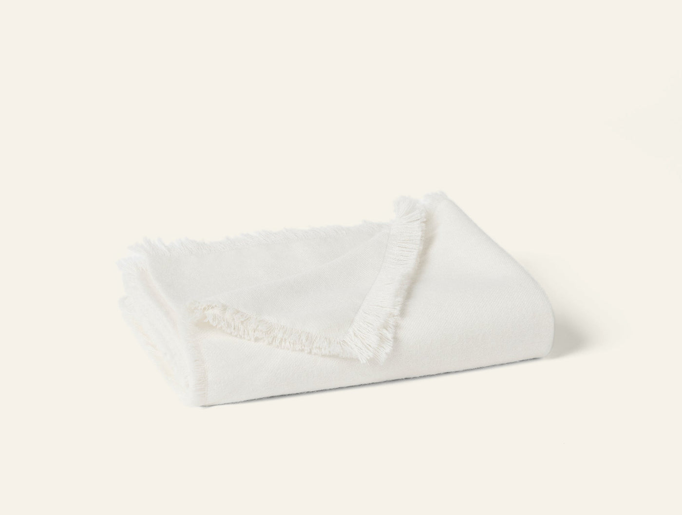 Folded ivory alpaca throw with delicate fringe trim, angled view on light background.