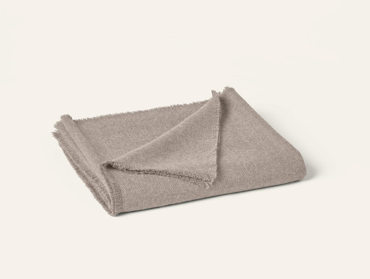 Folded taupe alpaca throw with fringe trim detail, soft textured weave visible at corner fold.