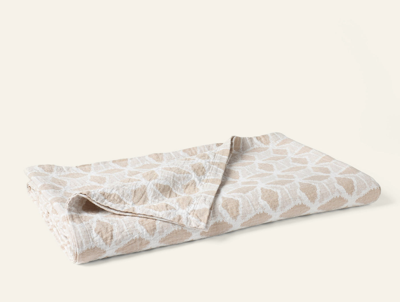 Coyuchi Palomar blanket in sand, folded flat, featuring a geometric ikat-style pattern.