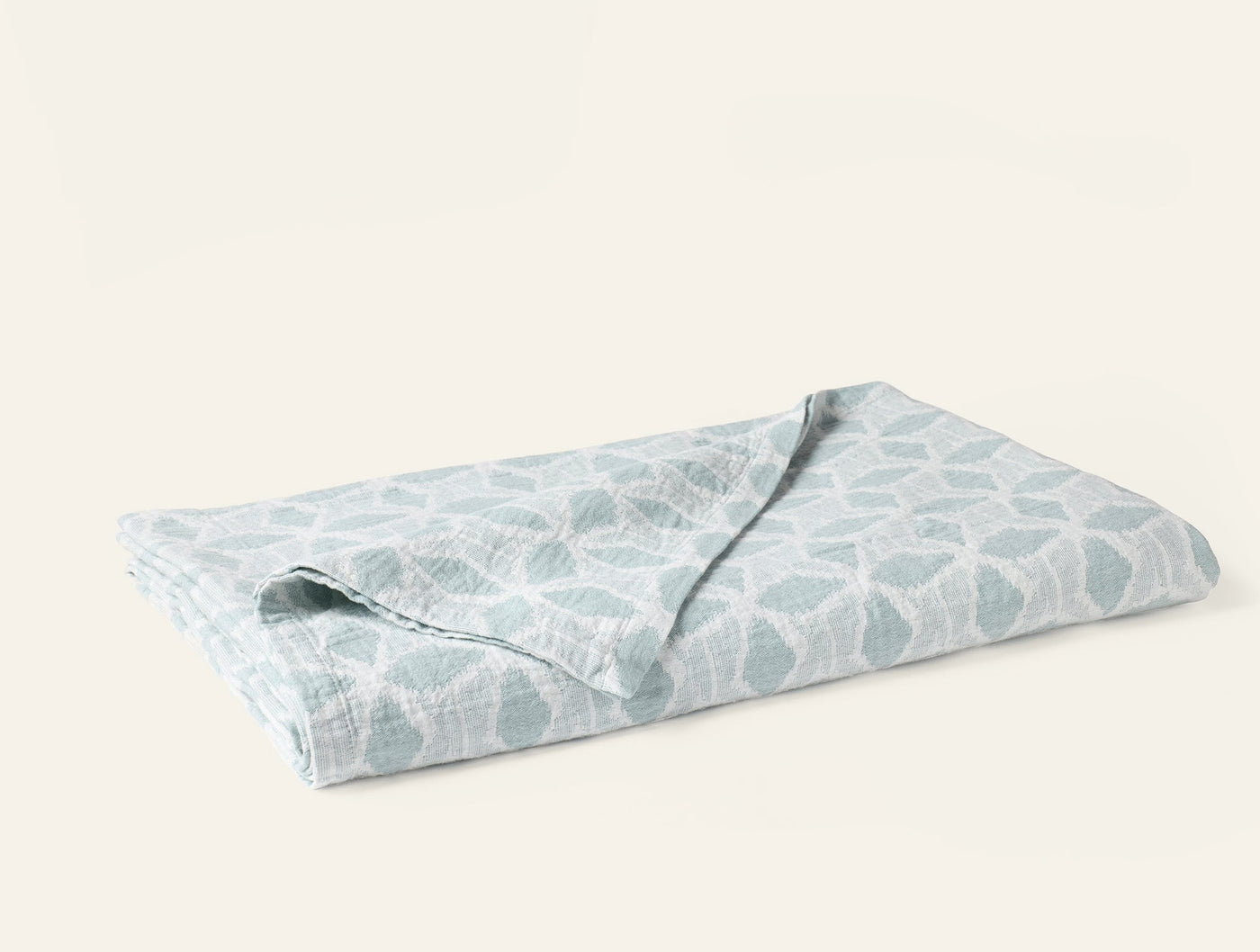 Close-up of folded Coyuchi Palomar blanket in seafoam with organic leaf print.