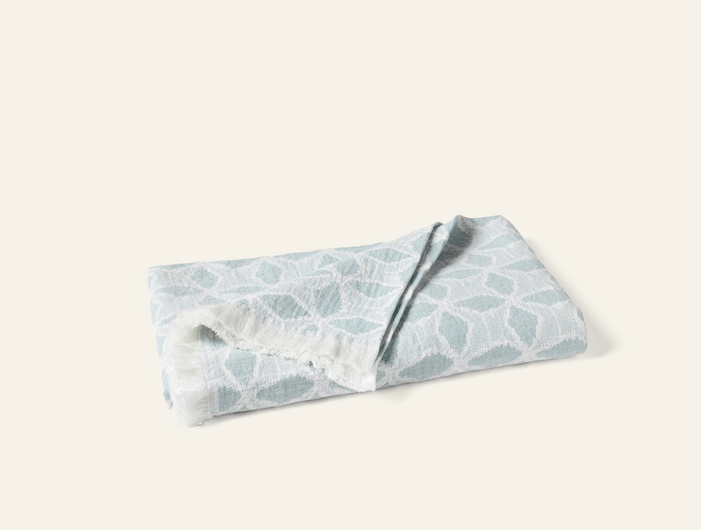Folded Coyuchi Palomar throw showing seafoam geometric leaf jacquard pattern and fringe edge.