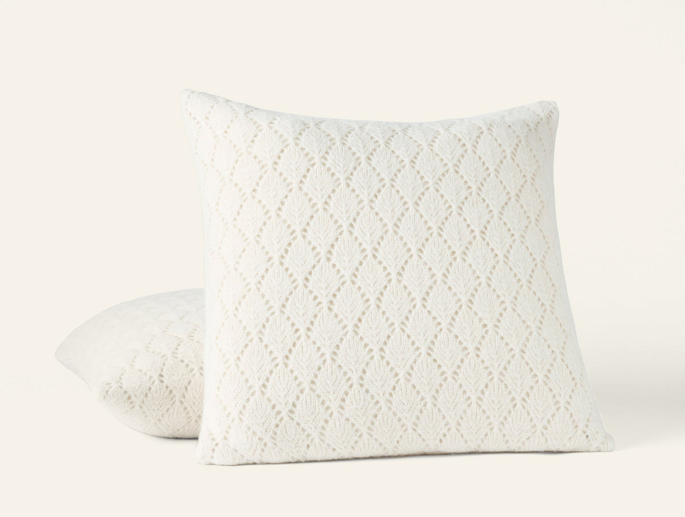 Two ivory Coyuchi Paracas pillows stacked, showing open-knit diamond pattern texture.