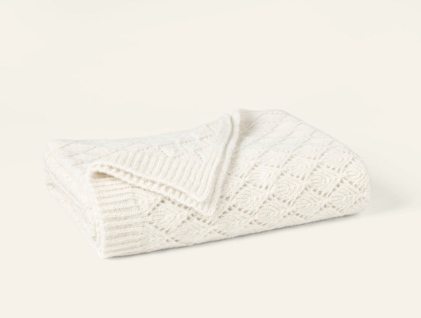 Close-up of ivory alpaca-cotton knit throw folded, showing diamond and eyelet stitch pattern.