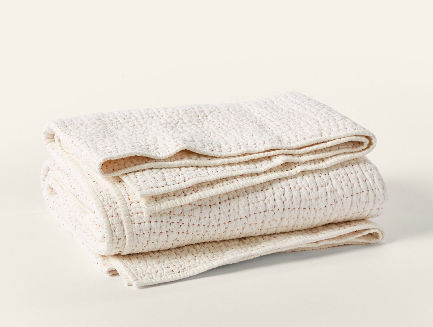 Coyuchi Pebbled Handstitched quilt folded, showing ivory textured weave and stitched hem detail.