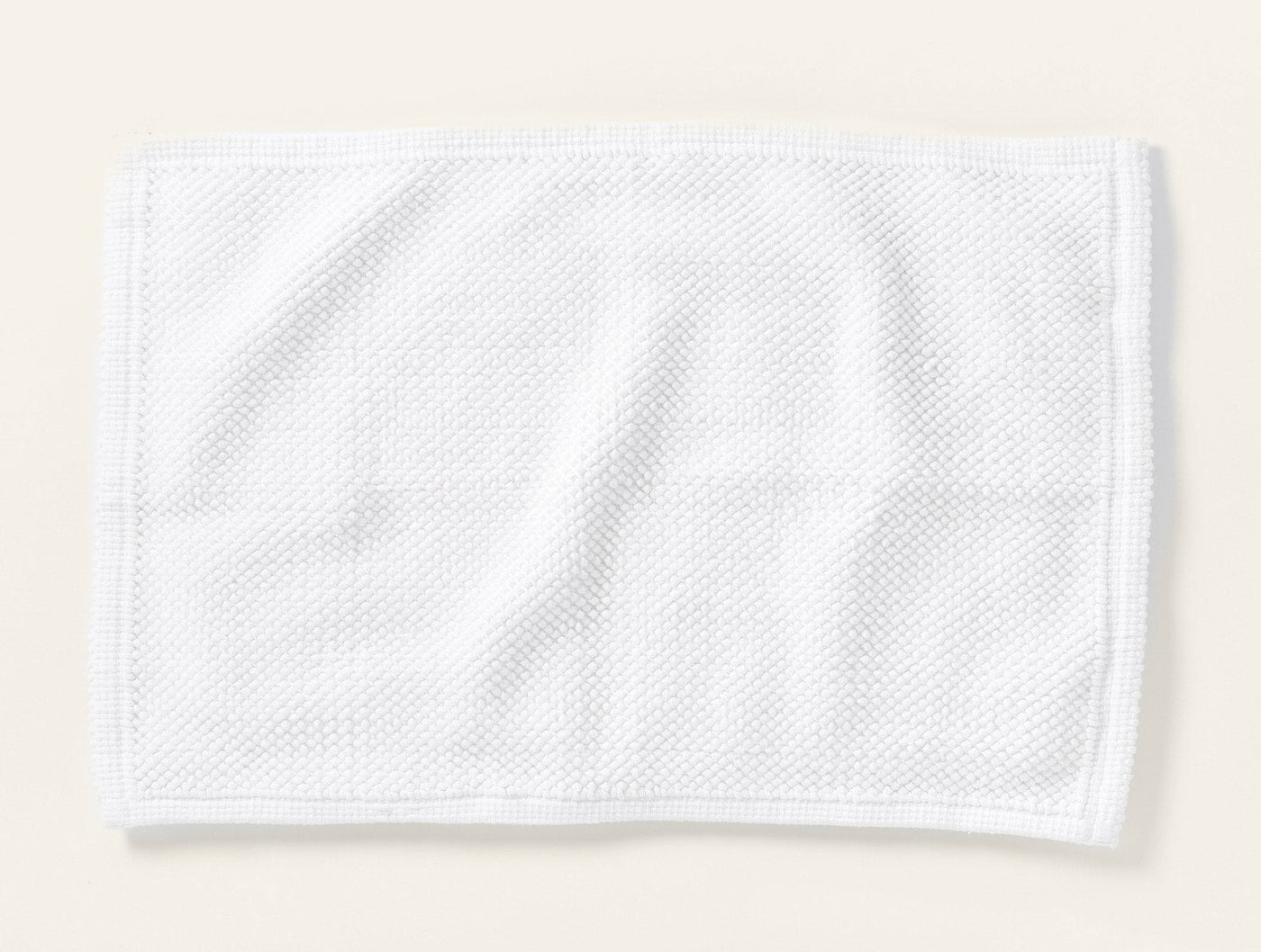 Coyuchi Pebbled bath rug in white with textured waffle weave, flat lay view.