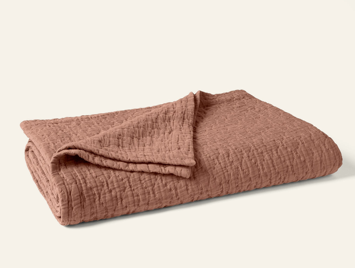 Coyuchi Pescadero Matelassé blanket folded, terracotta with textured woven surface.