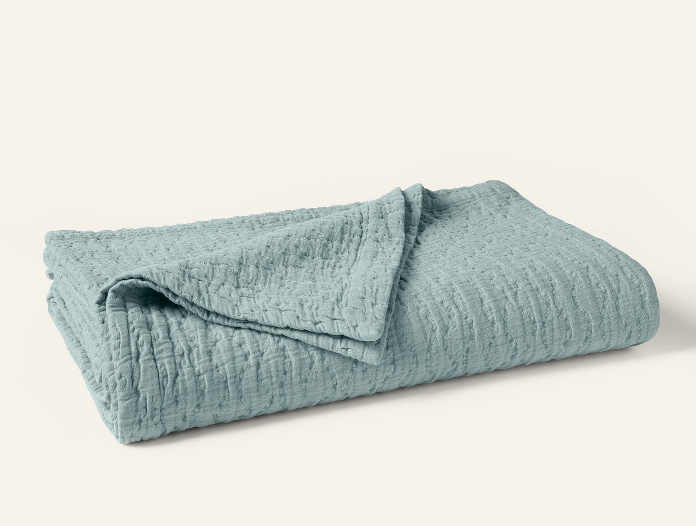 Coyuchi Pescadero Matelassé blanket folded, seafoam blue with textured wave pattern.