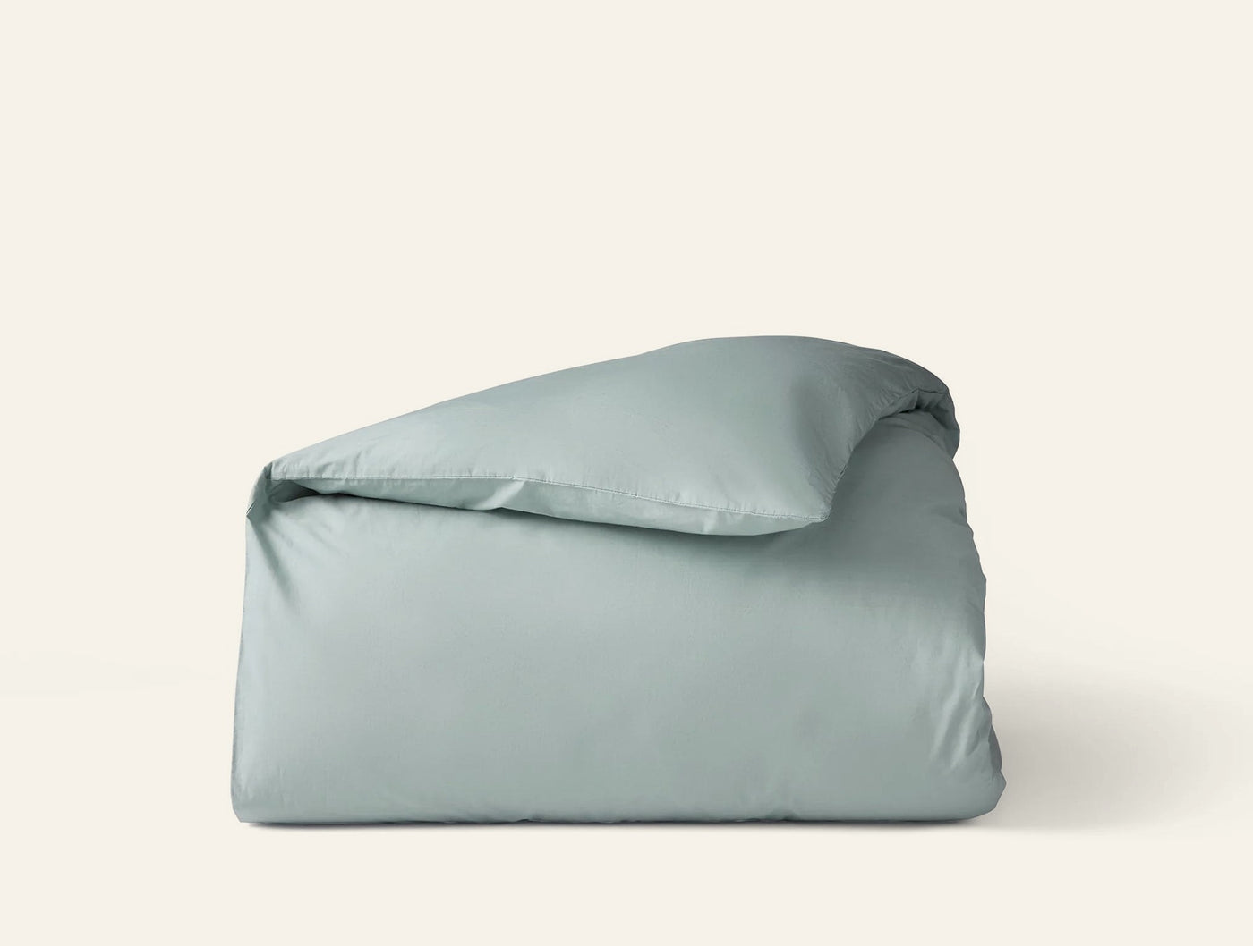 Folded Coyuchi Refined Percale duvet cover in sage, shown from a slight angle.