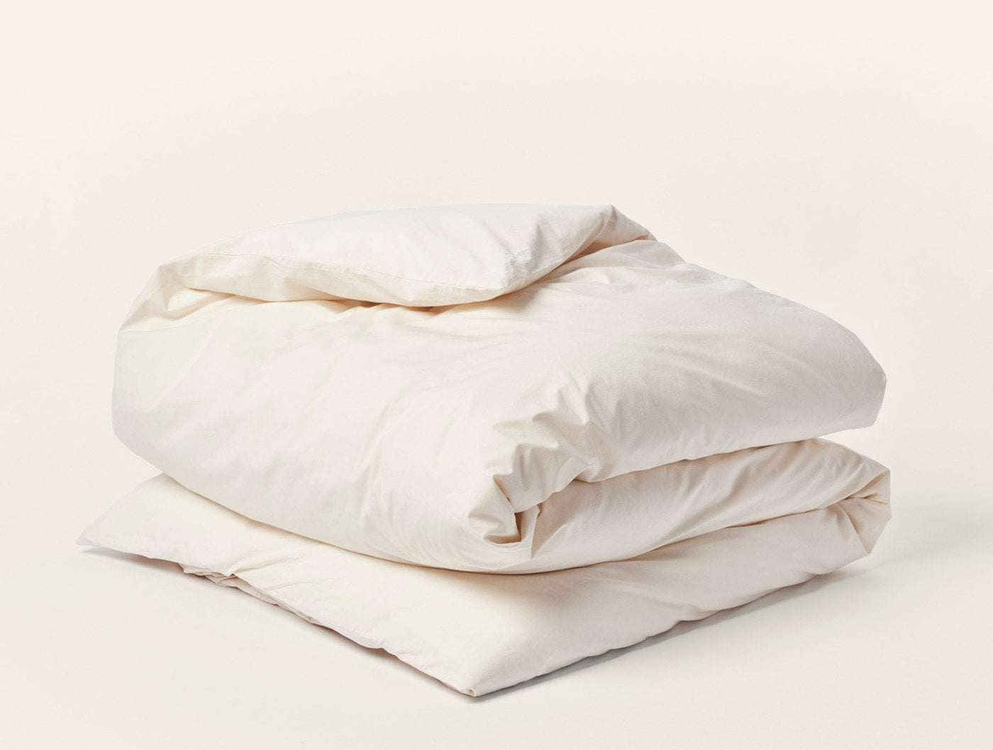 Ivory percale duvet cover folded and stacked, showing natural off-white tone and soft drape.