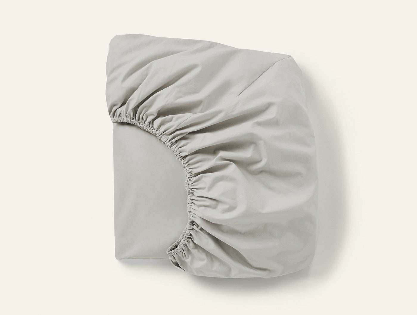 Coyuchi Refined Percale fitted sheet folded, showing elasticated corners in pale silver-grey.