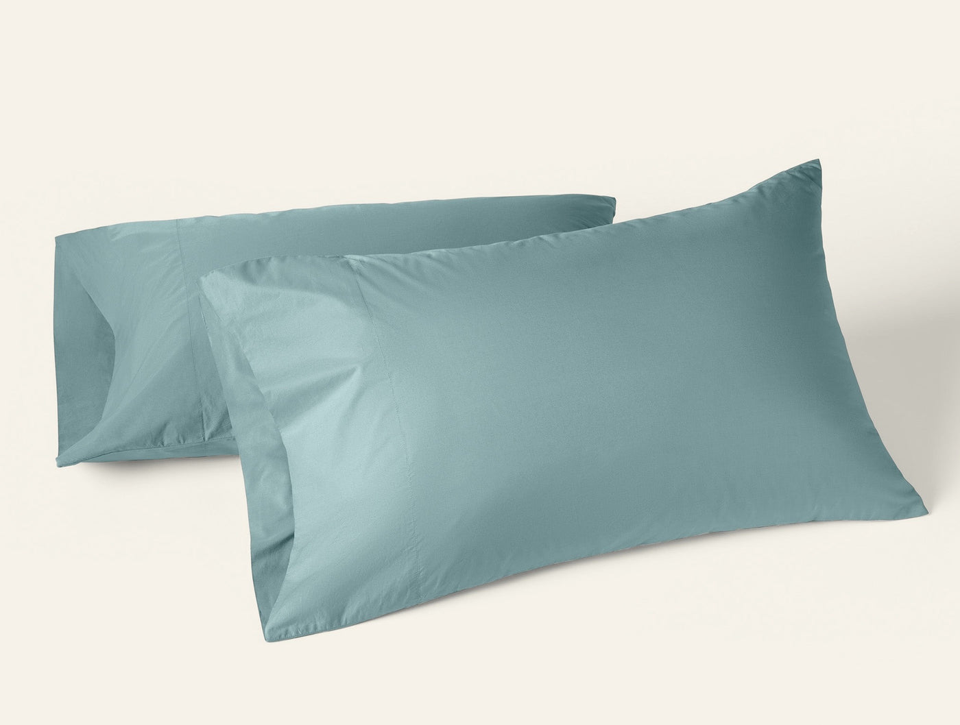Two Coyuchi Refined Percale pillowcases in muted teal, displayed upright against white background.