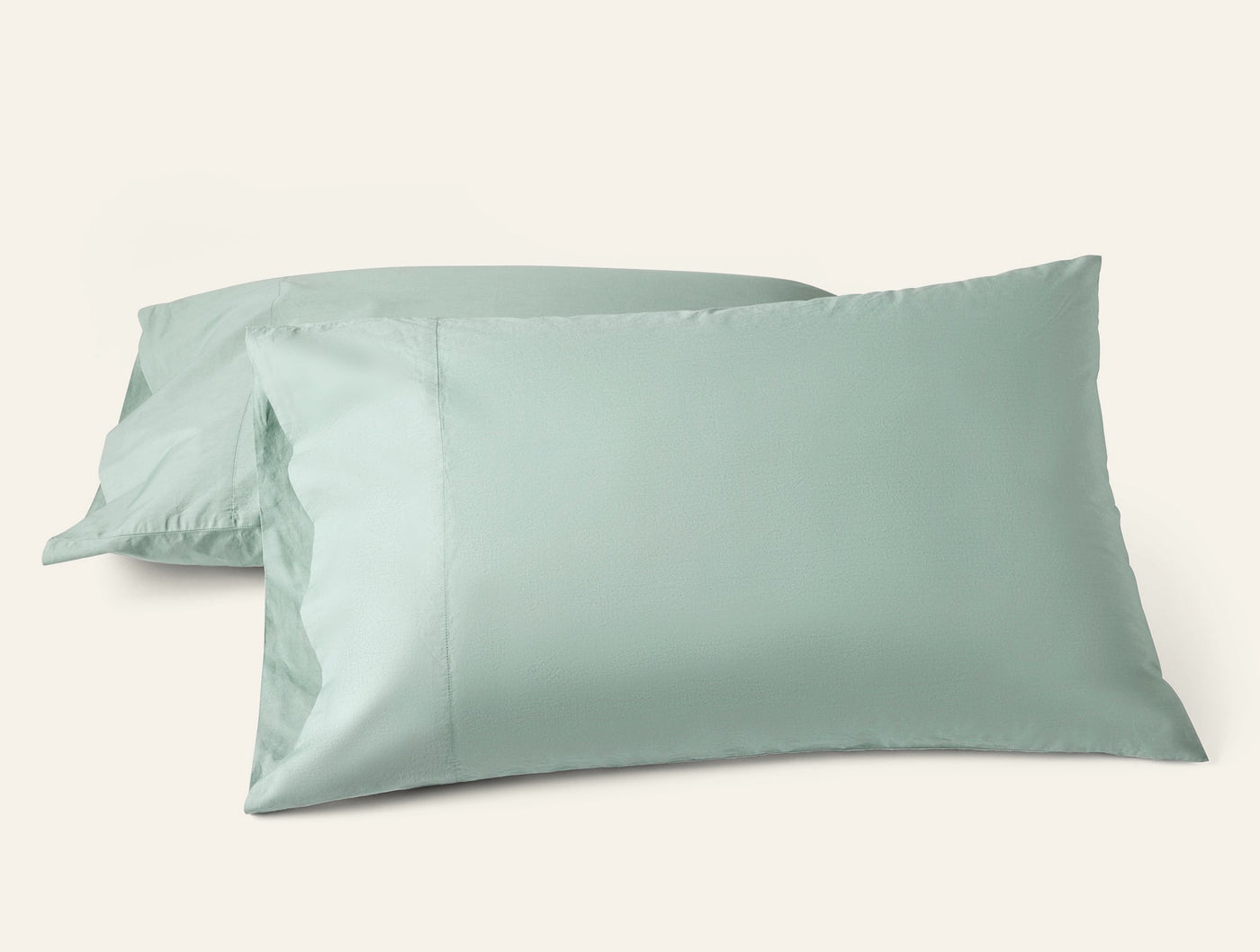 Two sage green Coyuchi Refined Percale pillowcases stacked against a white background.
