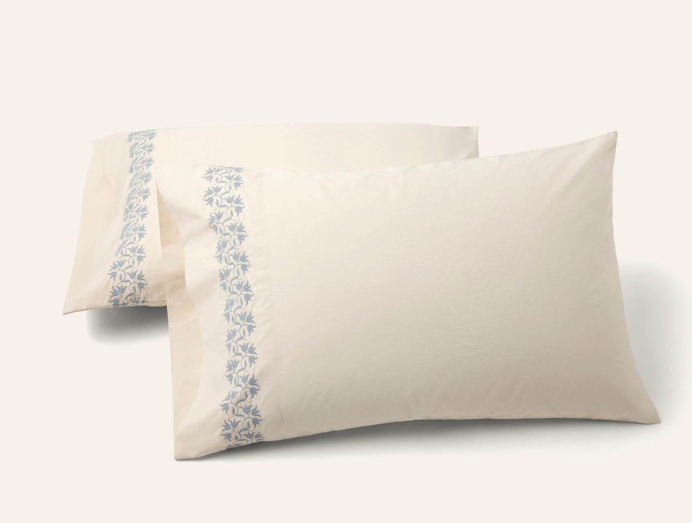 Pair of ivory Coyuchi Refined Percale pillowcases with blue floral embroidered border trim.