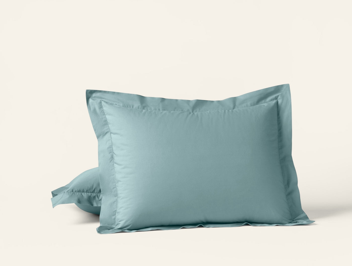 Sage green percale pillow shams stacked, showing tailored flange border detail.