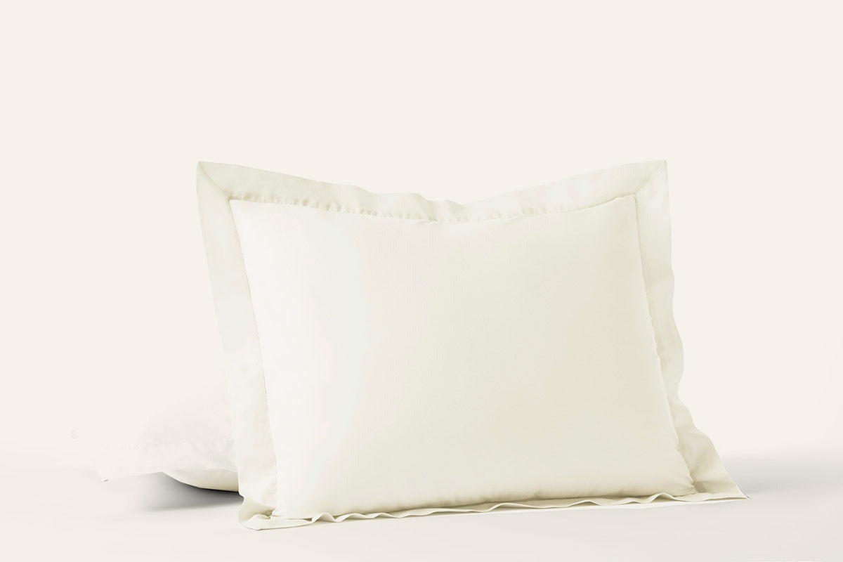 Ivory percale pillow shams with flange trim, stacked pair on white background.