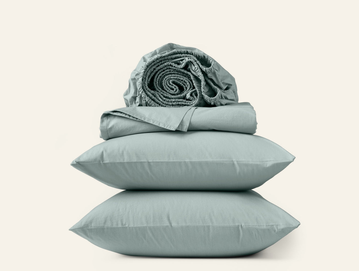 Sage green percale sheet set with two stacked pillowcases and rolled sheets on top.