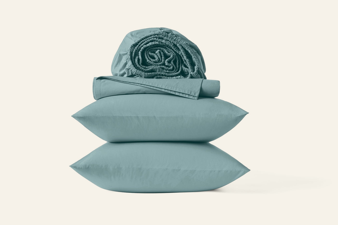 Close-up of stacked Coyuchi Refined Percale pillowcases and rolled sheets in sage green.
