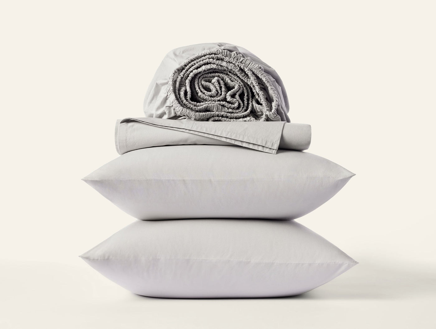 Stacked silver pillowcases with folded and rolled percale sheets on white background.