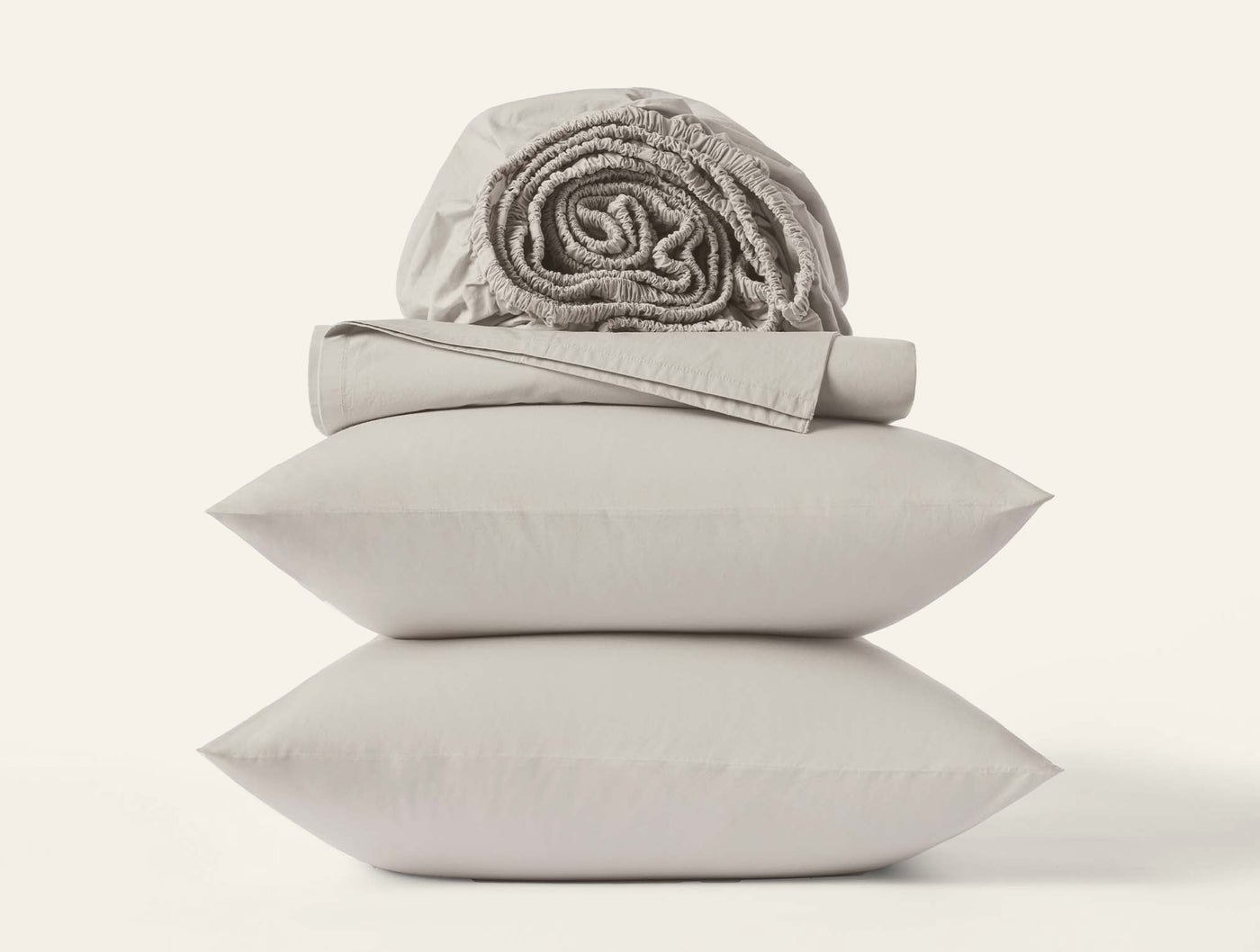 Stacked pillowcases with folded flat sheet and rolled fitted sheet in warm grey percale.