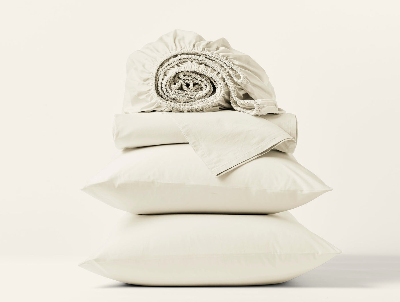 Close-up of stacked ivory Coyuchi Refined Percale pillowcases and rolled fitted sheet.