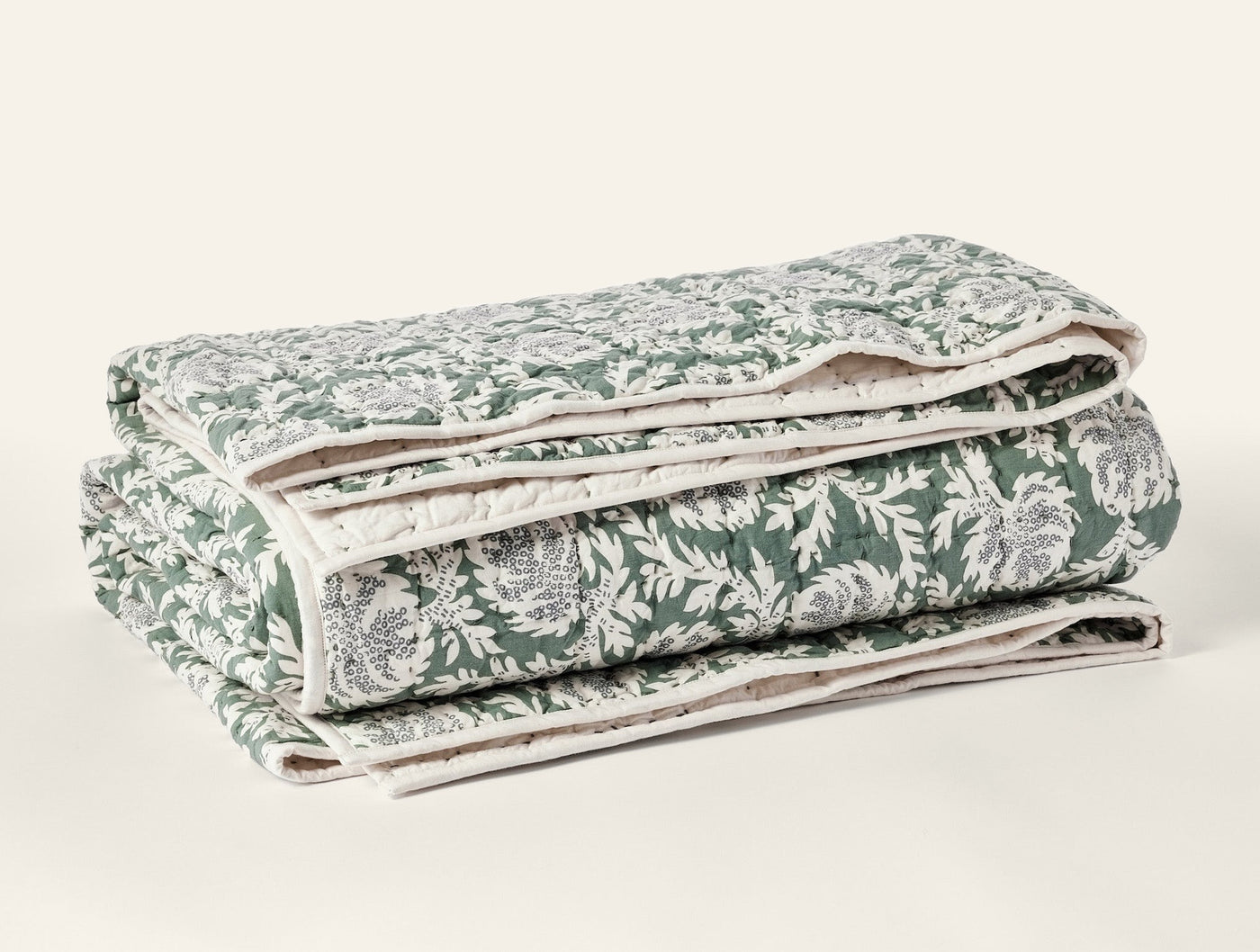 Folded Coyuchi quilt showing green and ivory floral block-print pattern and handstitched edges.