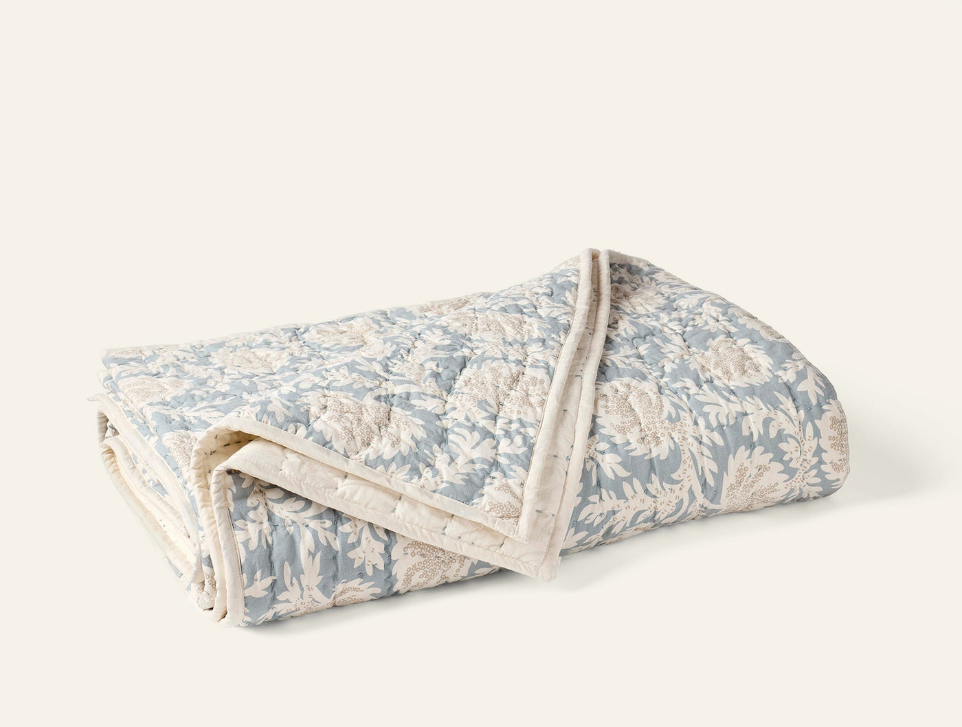 Folded Coyuchi Robles quilt showing dusty blue floral block-print pattern and ivory scalloped trim.