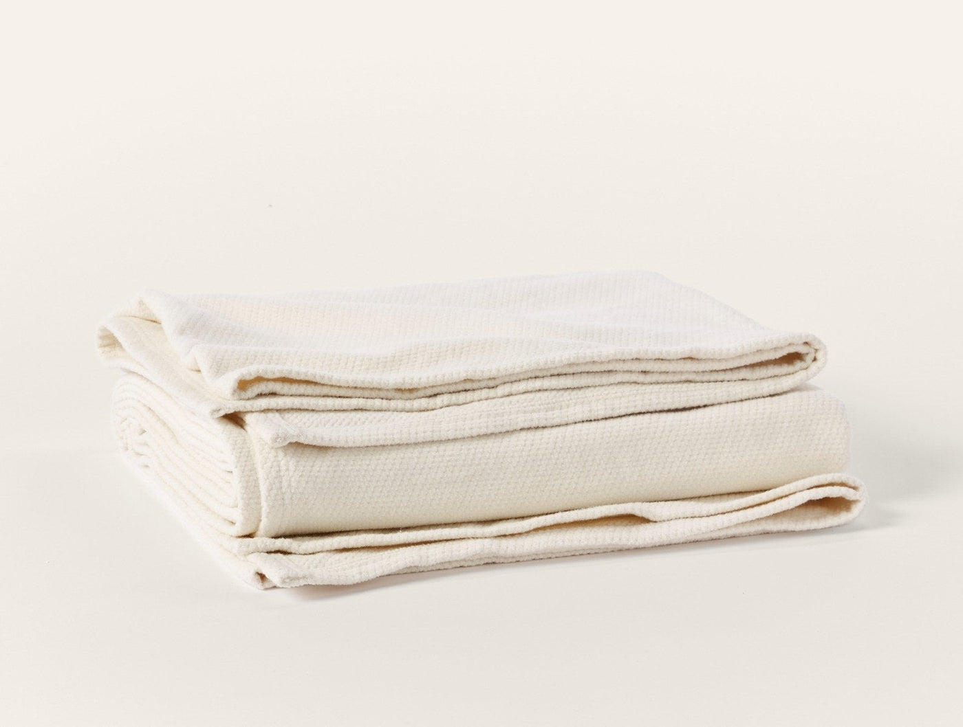 Ivory woven blanket folded to show textured weave and finished edges.