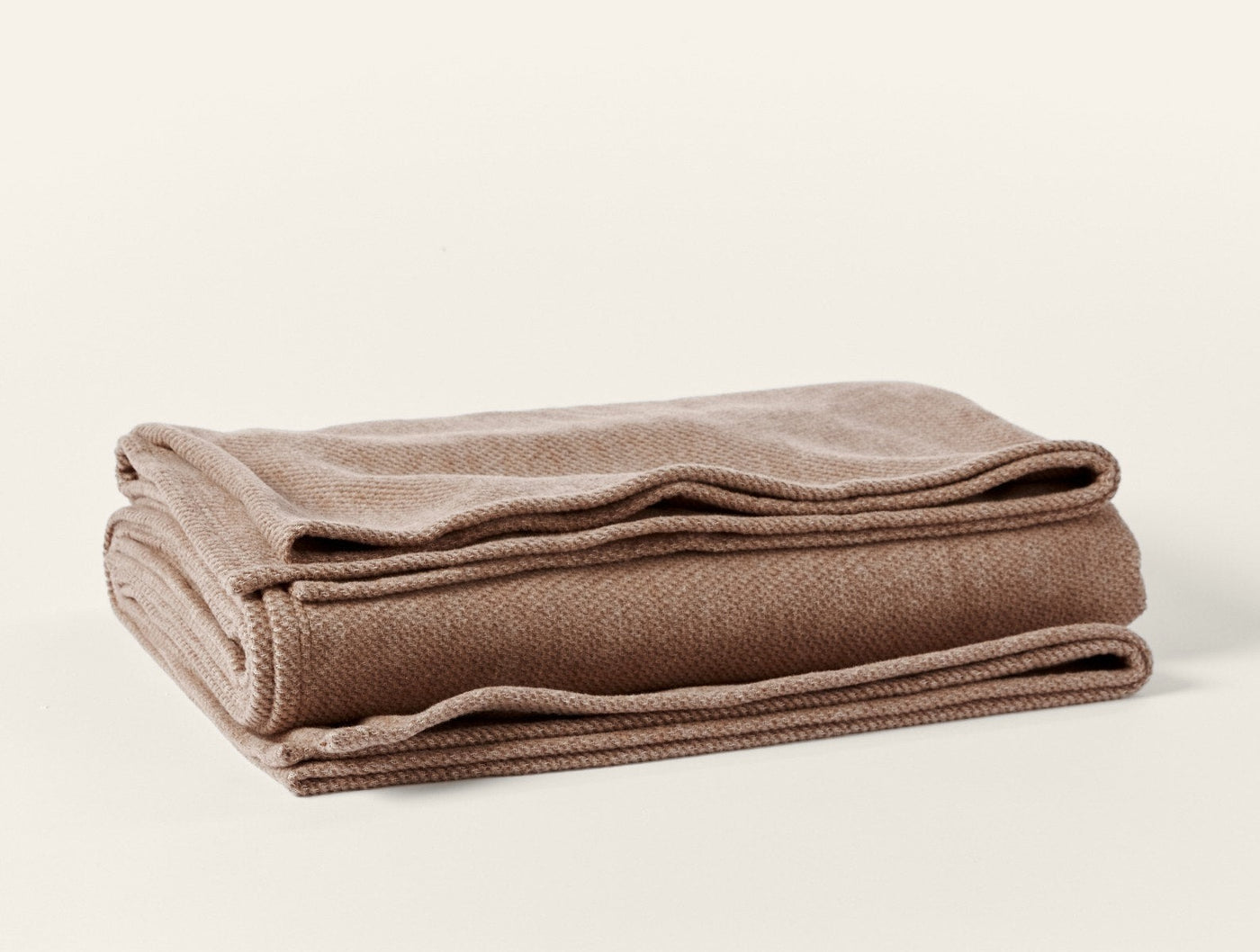 Folded camel herringbone-weave throw, showing thick edge hem detail.