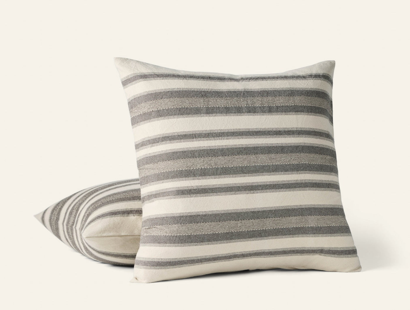 Two Coyuchi Serrano pillows stacked, ivory and grey woven stripes, textured linen front face.