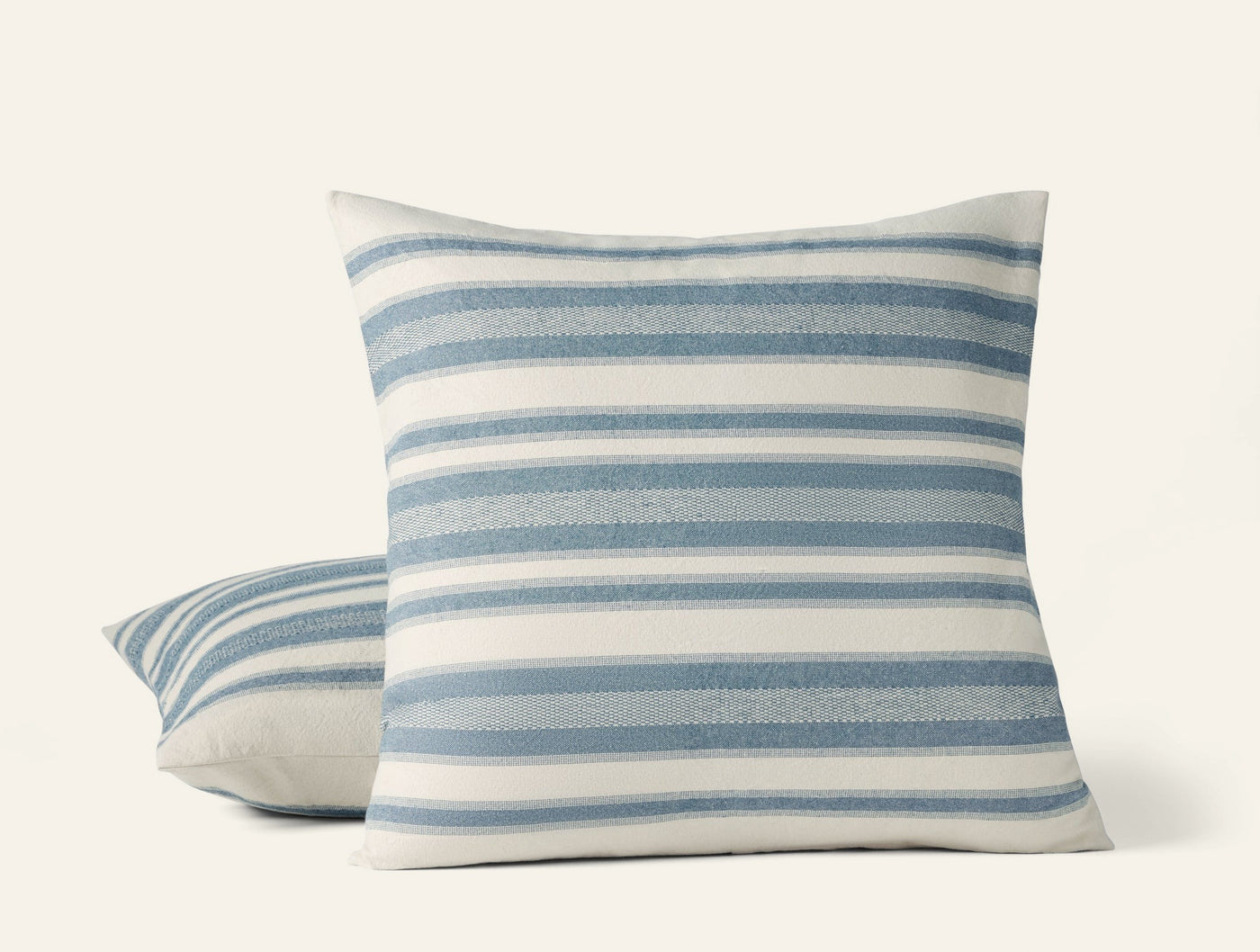 Close-up of two Coyuchi Serrano pillow covers with blue and ivory horizontal stripes.