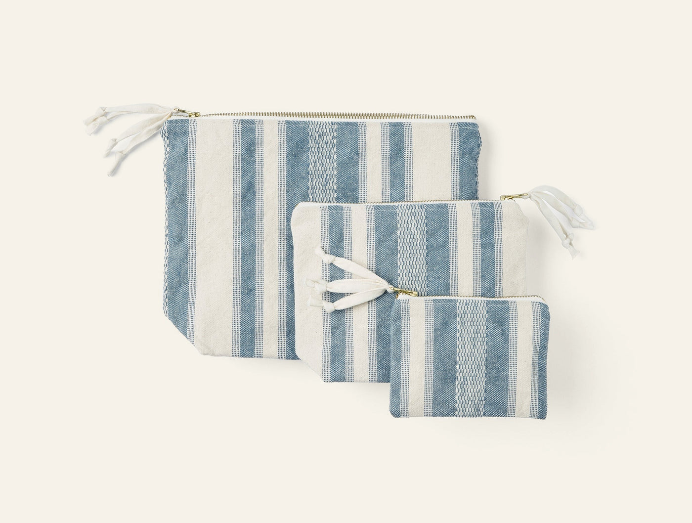 Three Coyuchi Serrano pouches in varied sizes, blue and ivory stripe with gold zippers.