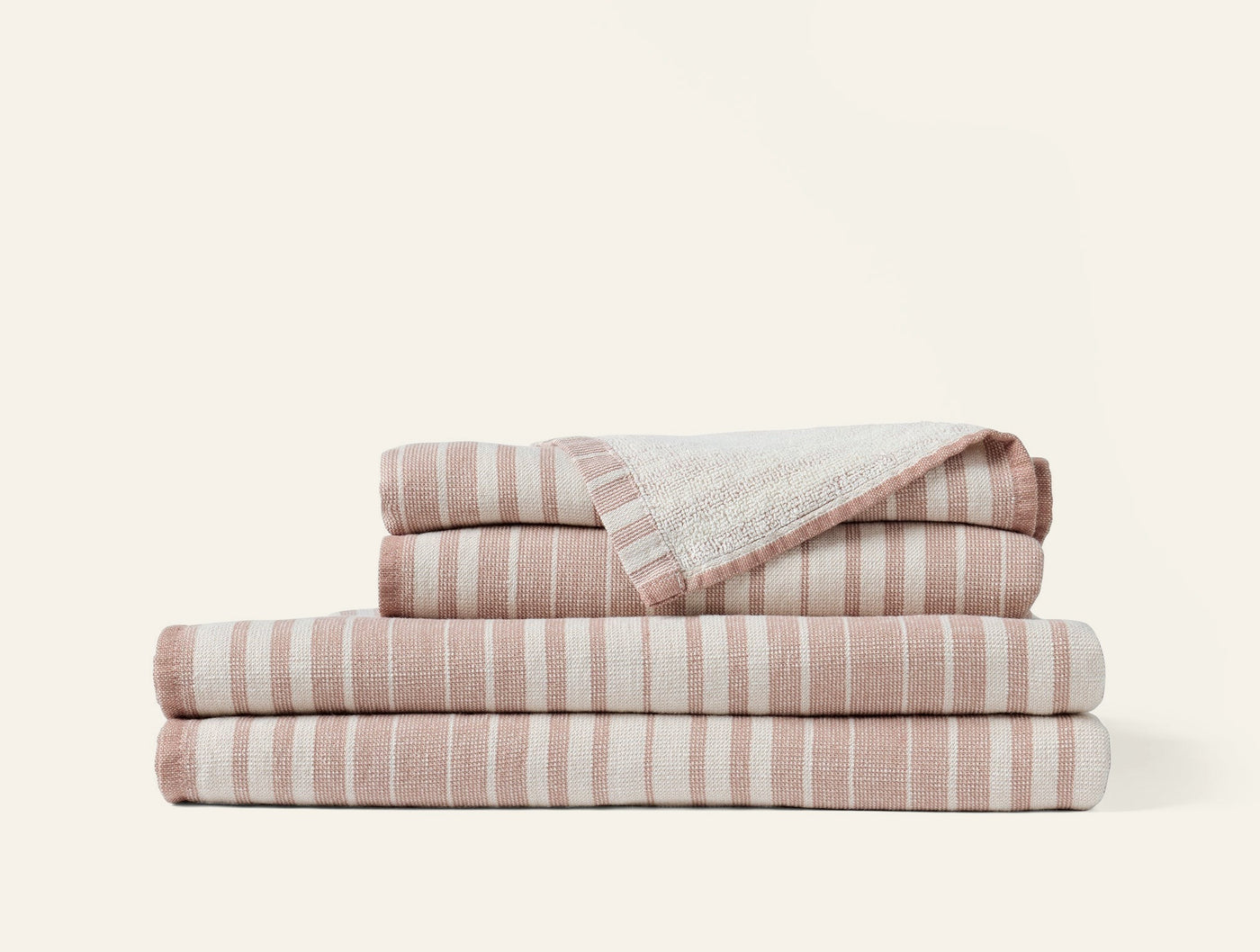 Folded stack of rose and ivory striped bath towels with fringed hem detail visible on top towel.