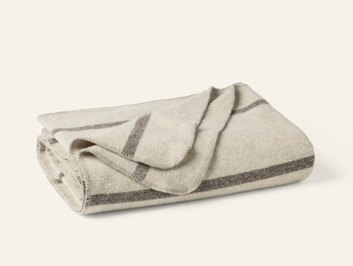 Folded ivory wool blanket with charcoal stripe border detail along edges.