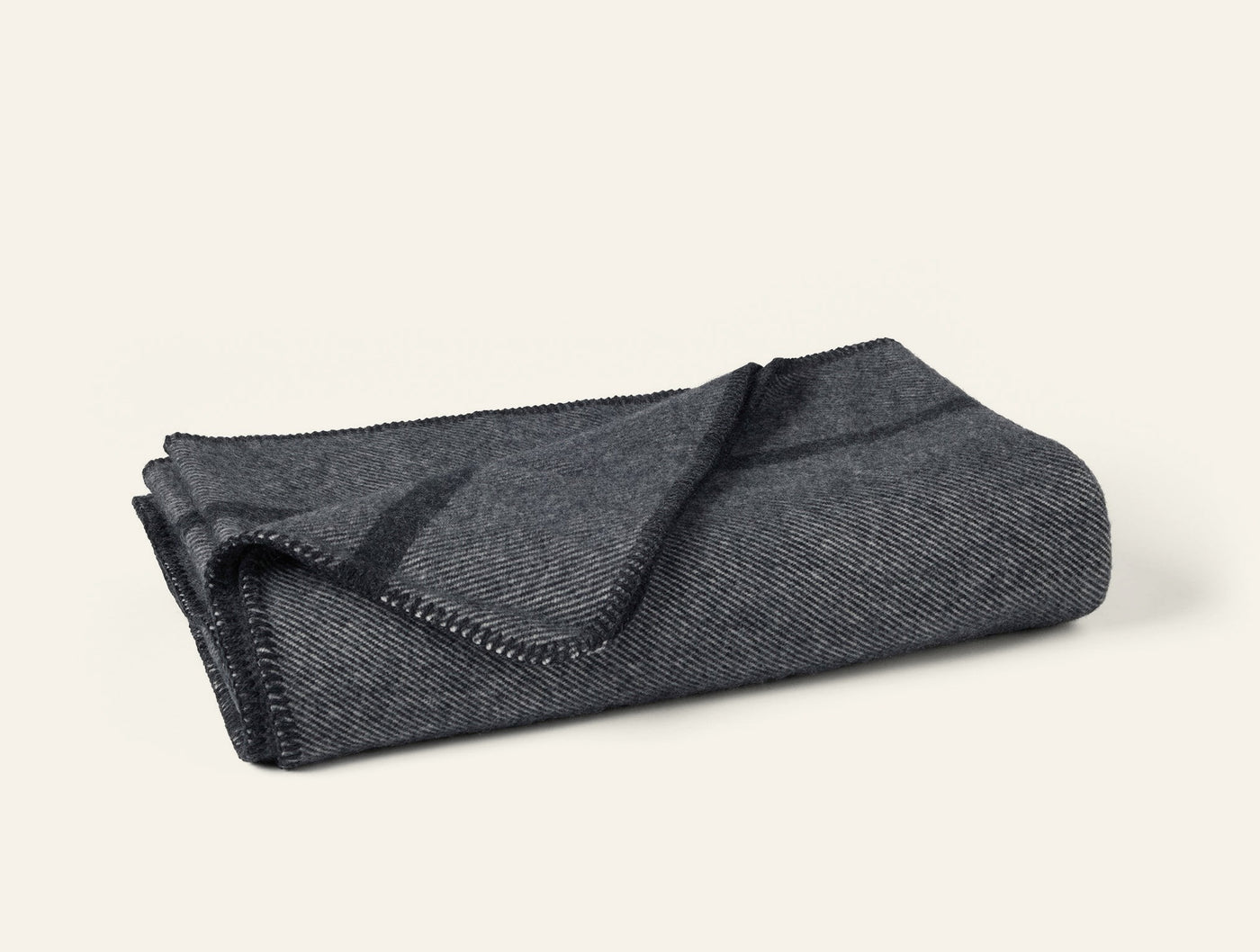 Close-up of folded Coyuchi Tahoe Wool throw in charcoal herringbone with blanket-stitch edge trim.