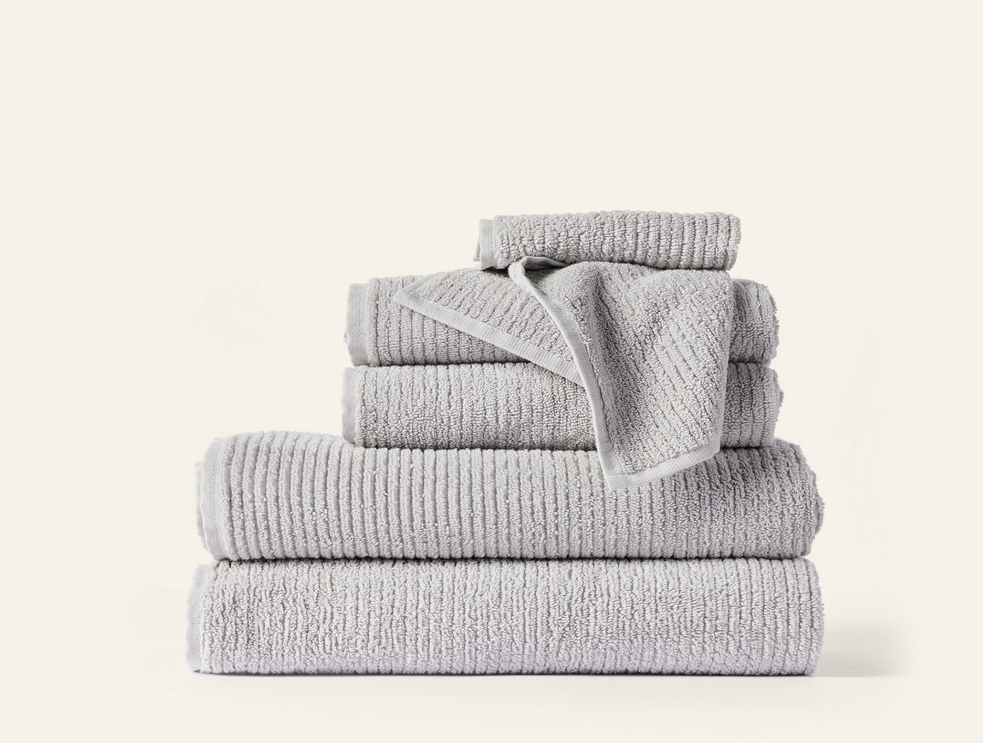 Stacked set of six silver ribbed cotton towels in varying sizes on white background.