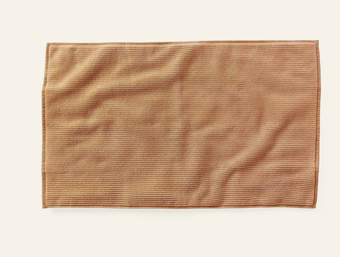 Coyuchi Temescal bath rug in warm caramel, showing ribbed texture and stitched border detail.