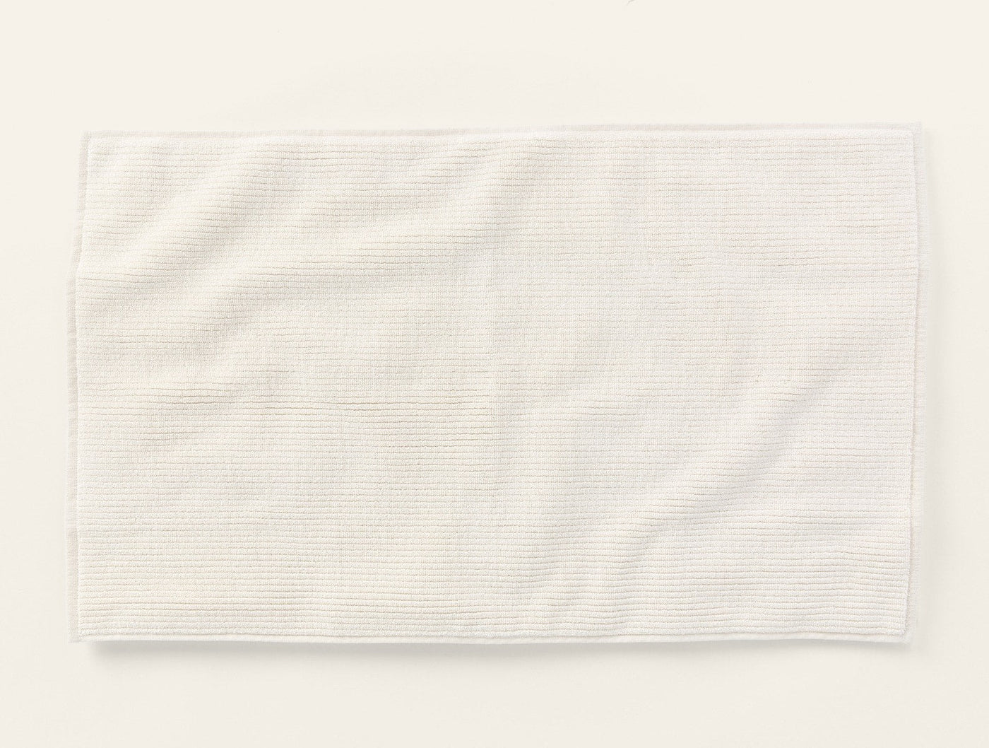 Coyuchi Temescal Ribbed bath rug in ivory, showing ribbed texture and draped flat lay.