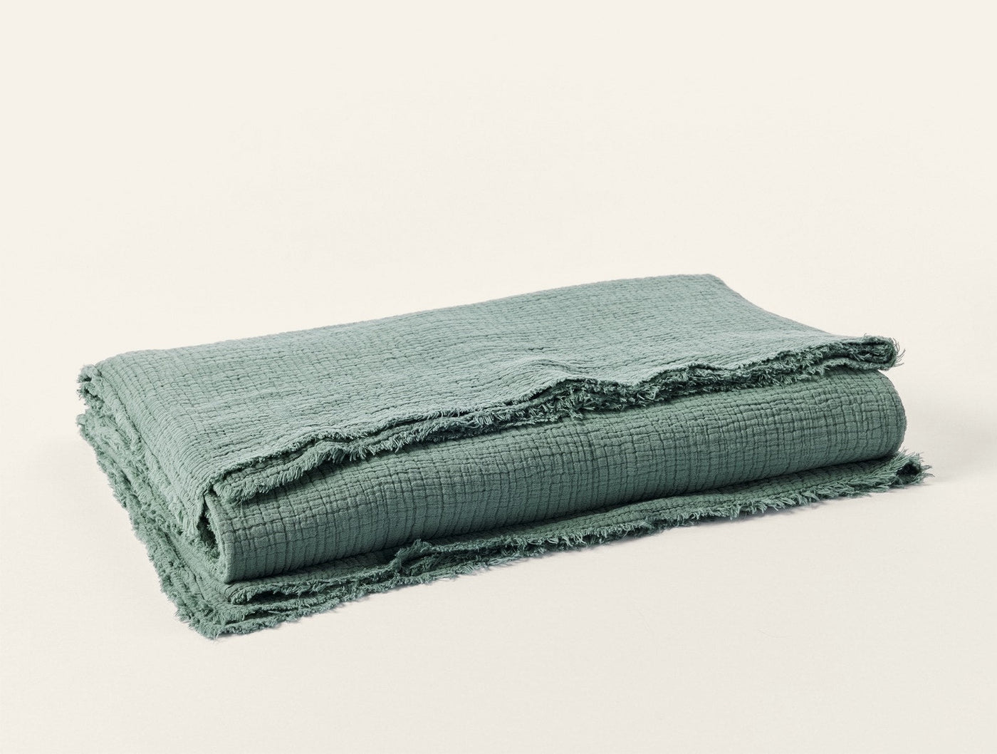 Close-up of sage green matelasse blanket folded, showing frayed edge trim detail.