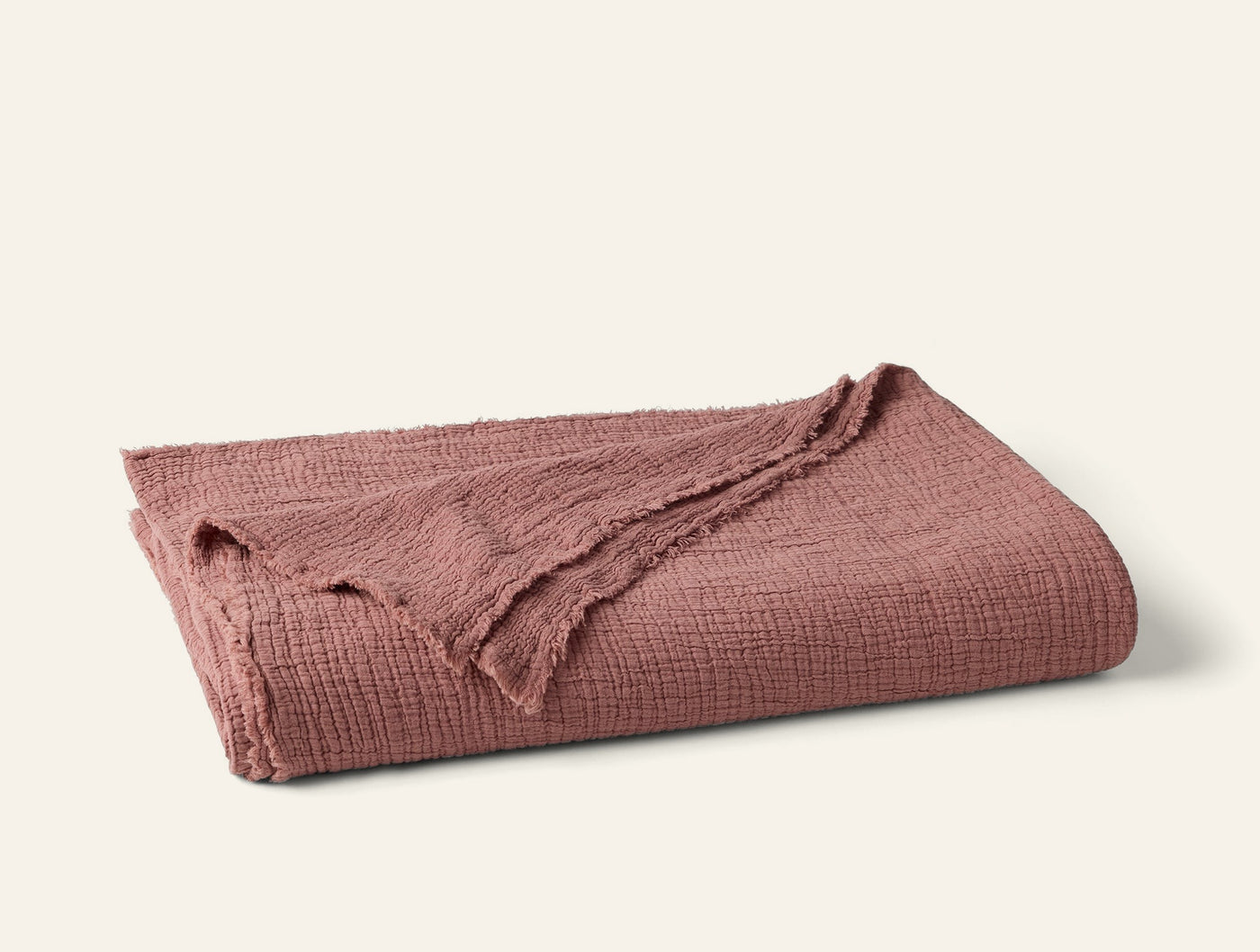 Folded Coyuchi Topanga Matelassé blanket in dusty rose with textured weave and fringe edge.