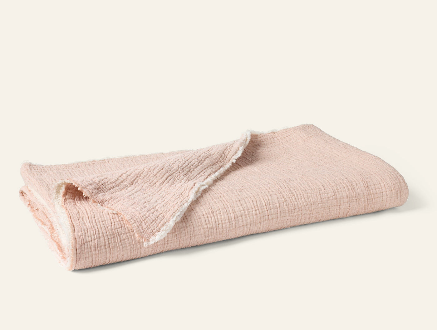 Folded blush matelassé blanket showing fringe edge detail against white background.
