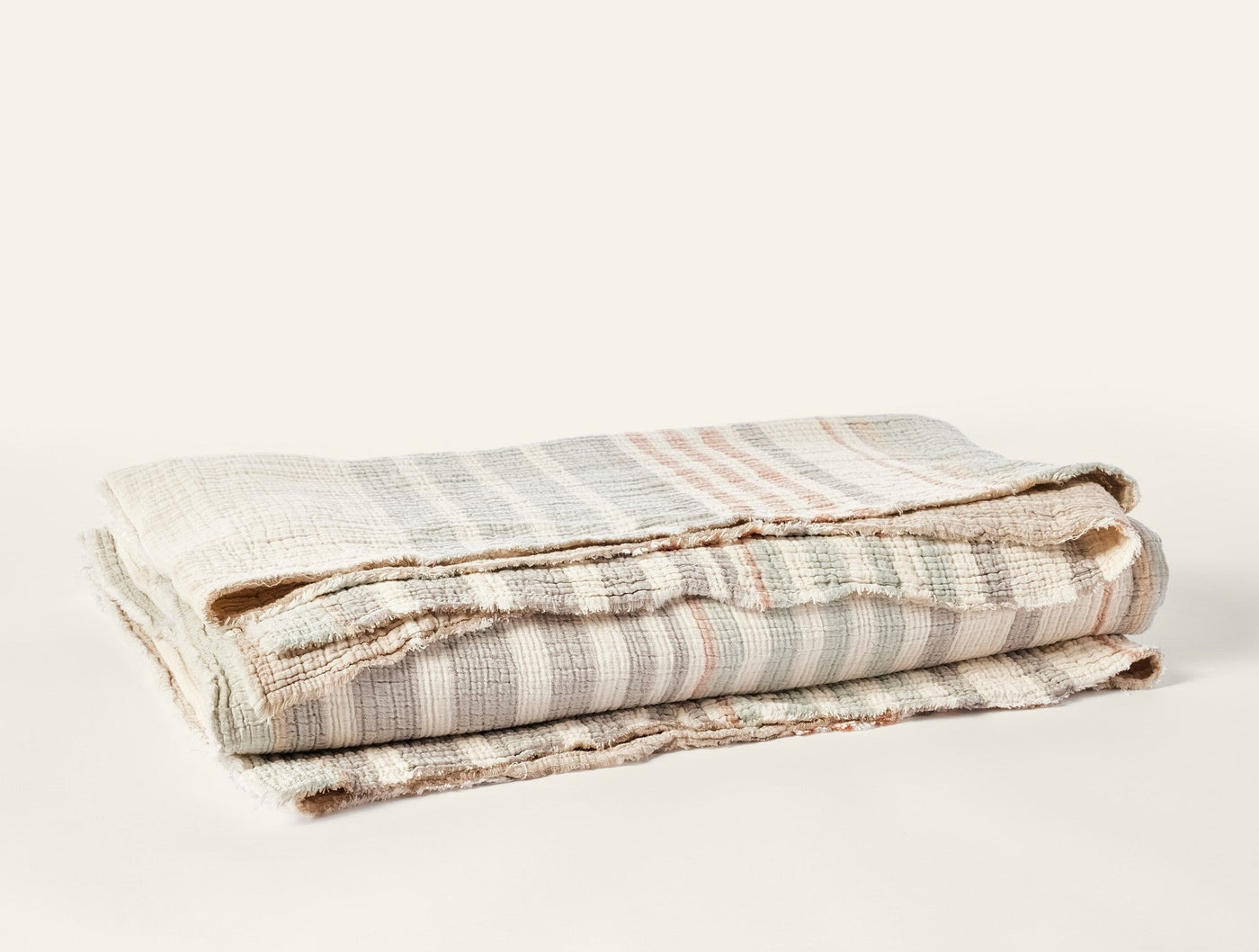 Close-up of folded Coyuchi Topanga Matelassé blanket showing striped weave texture in soft neutrals.