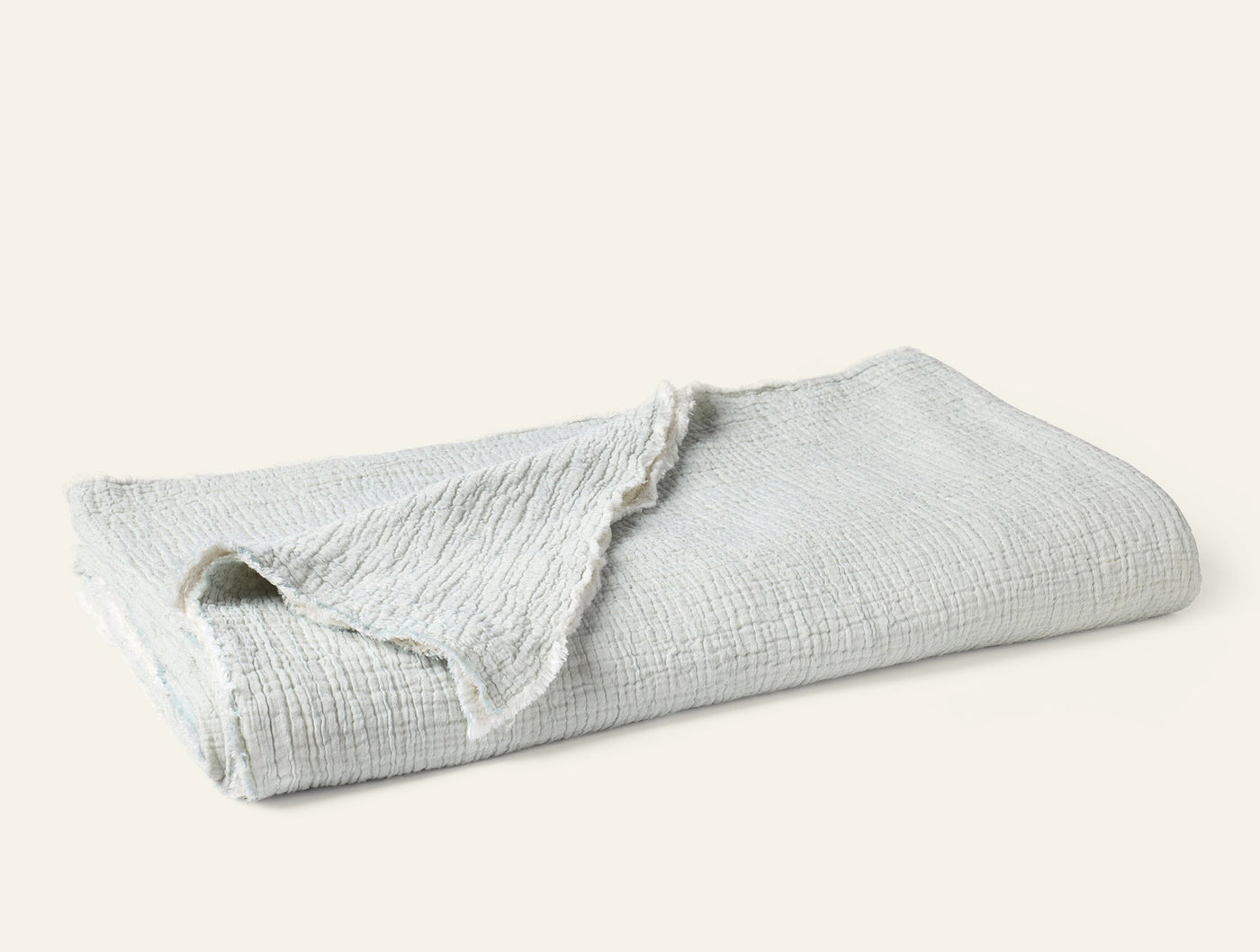 Folded ivory matelassé blanket with fringe trim, showing textured weave detail.