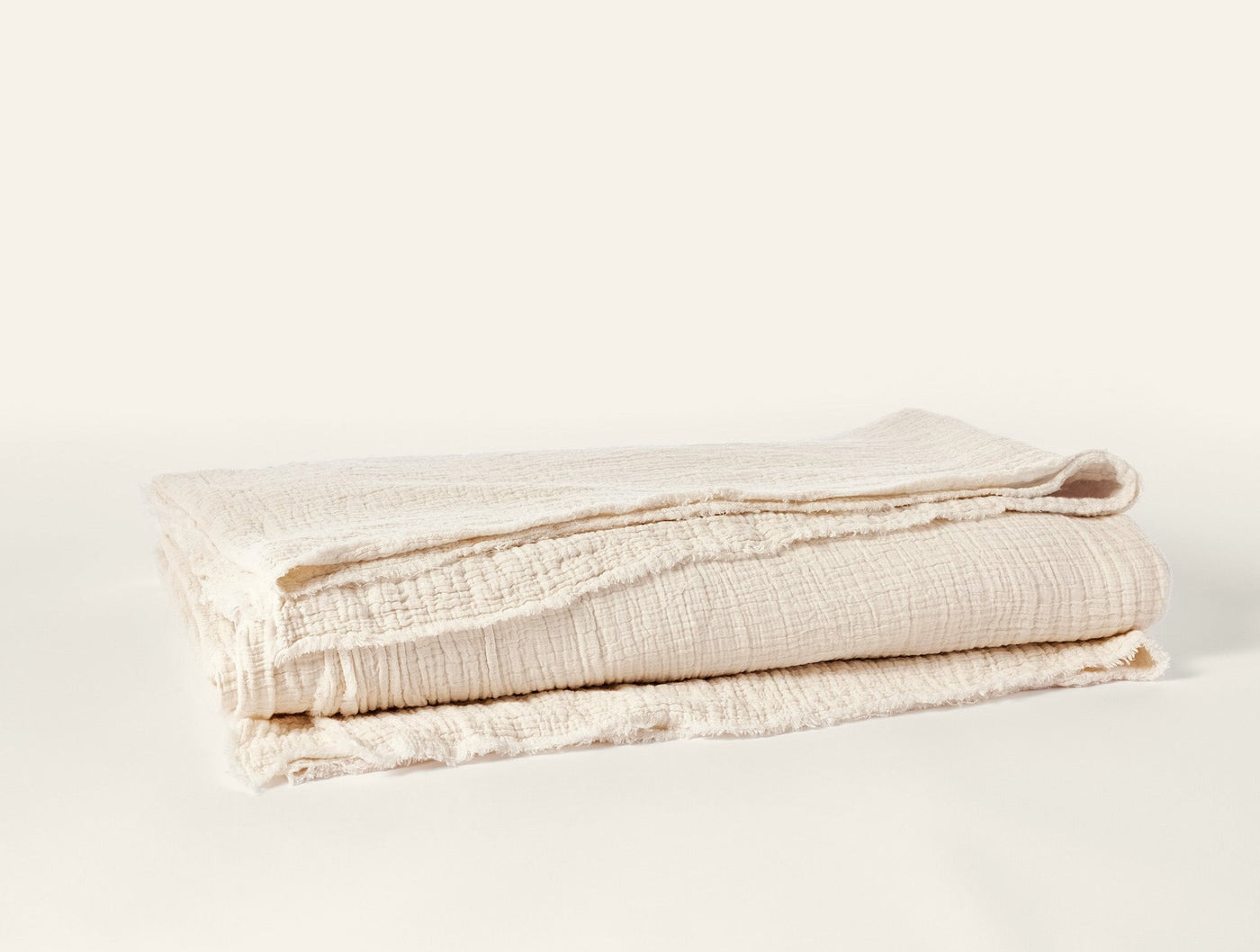 Folded ivory Coyuchi Topanga Matelassé blanket showing textured weave and fringe edge detail.