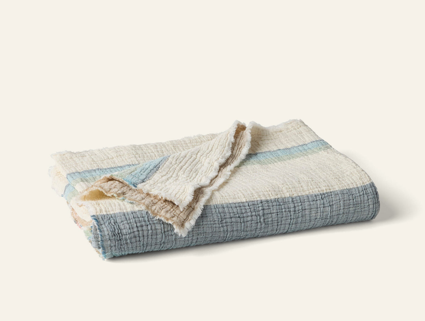 Coyuchi Topanga Matelasse throw folded, slate blue stripes with ivory fringe trim.