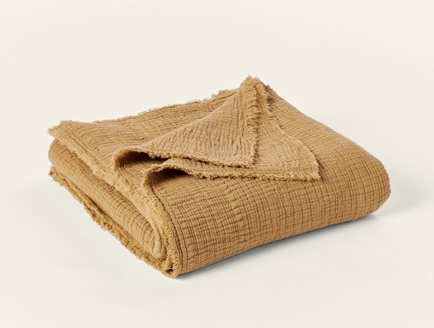 Folded mustard cotton matelassé throw with frayed edges, showing textured weave detail.