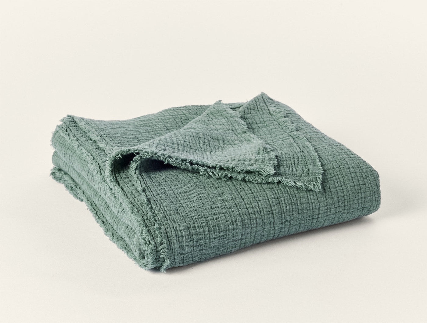 Coyuchi Topanga throw folded, sage green matelasse weave with fringe trim detail.