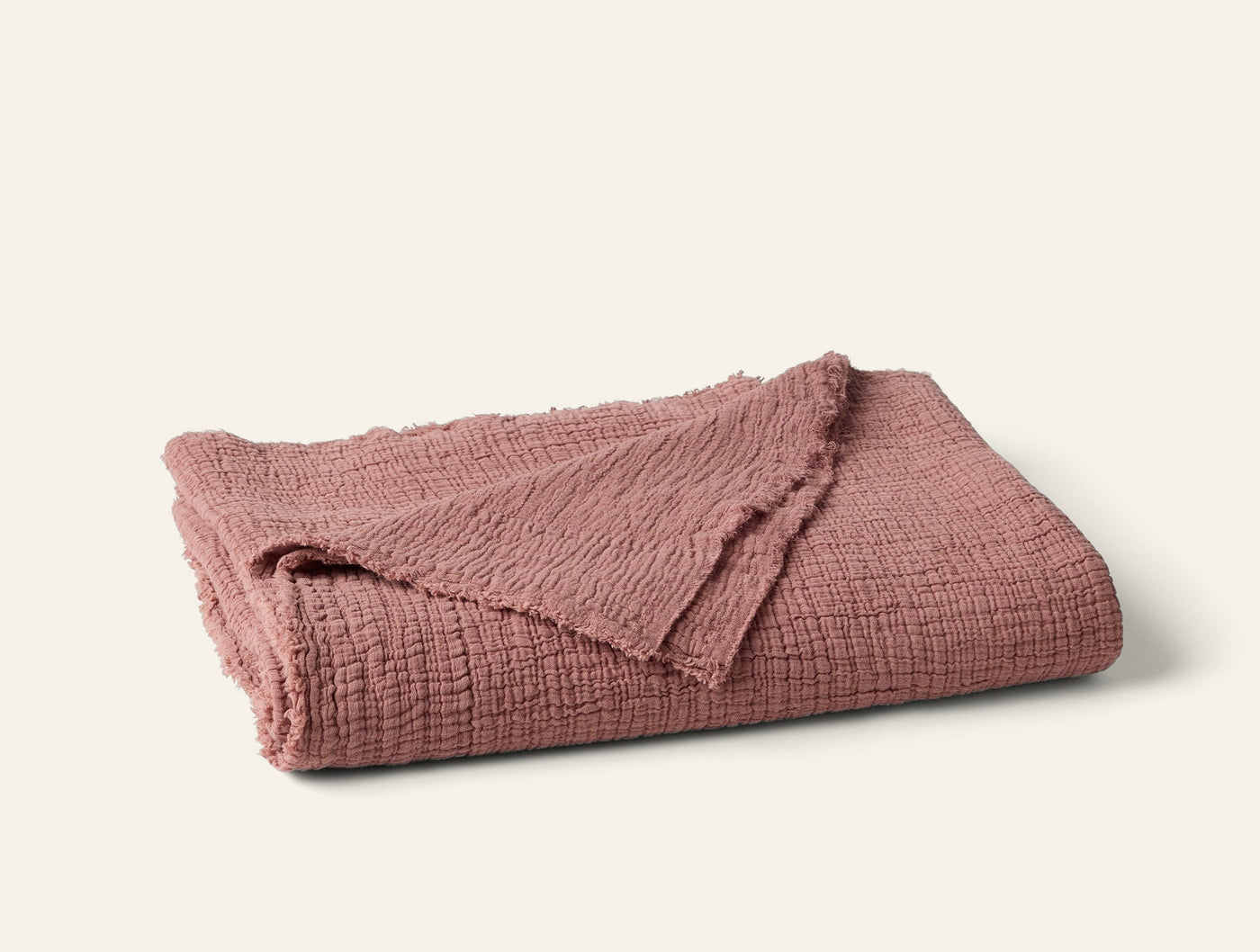 Folded rose Coyuchi Topanga Matelasse throw showing textured weave and frayed edges.